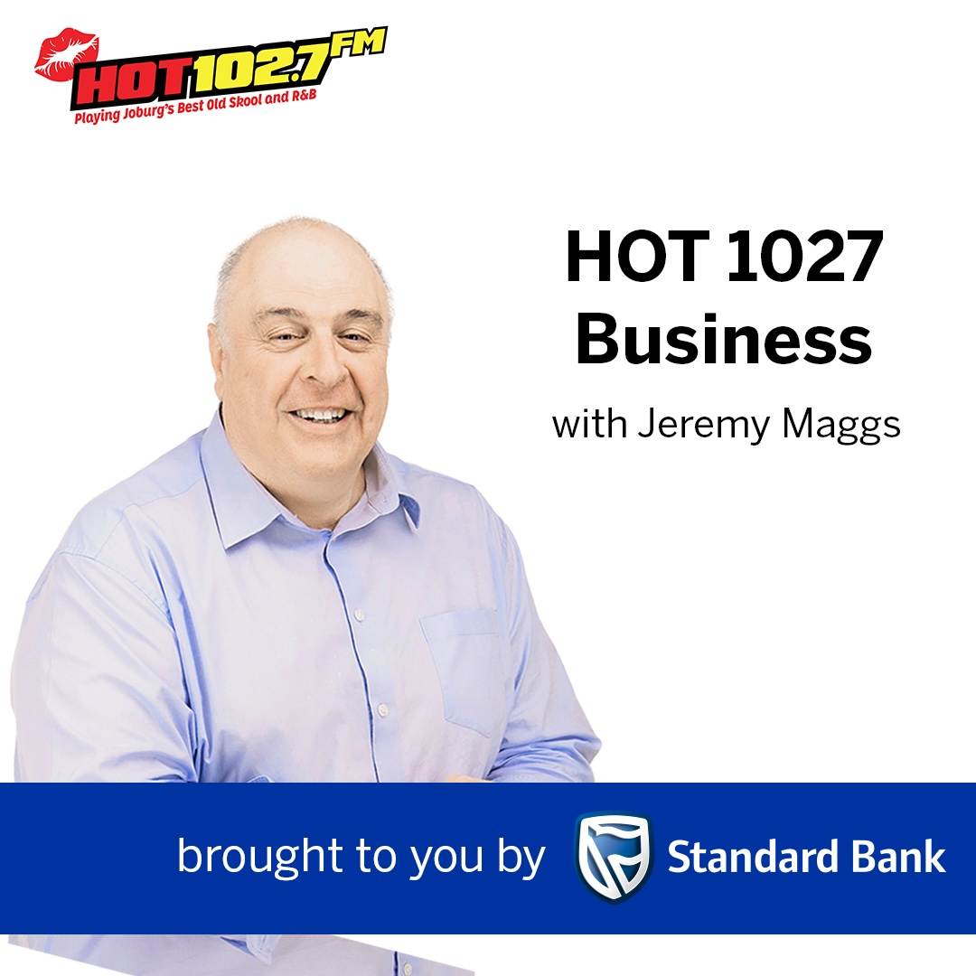 A man in a light blue shirt smiles at the camera. Text reads: HOT 1027 Business with Jeremy Maggs, and brought to you by Standard Bank. The HOT 102.7 FM logo is in the top left corner.