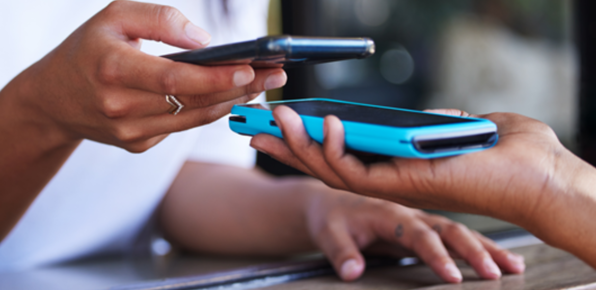 Two people exchange a digital payment by holding their smartphones close together over a wooden counter, highlighting the convenience of contactless transaction technology enabled by mobile banking.