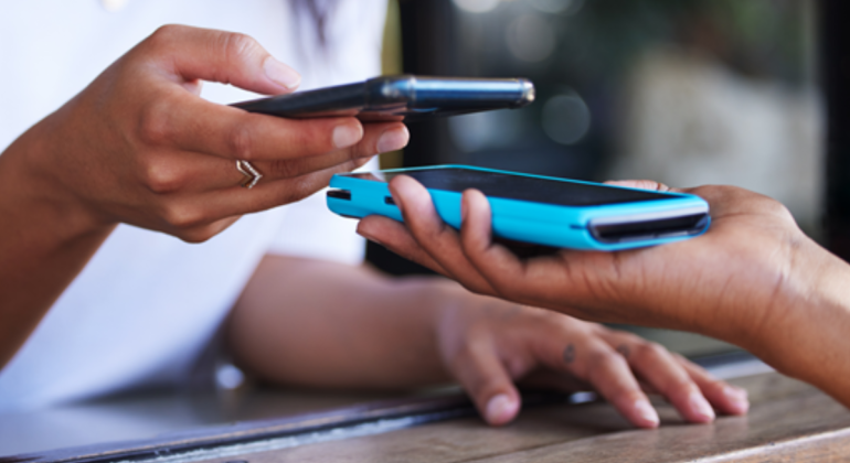 Two people exchange a digital payment by holding their smartphones close together over a wooden counter, highlighting the convenience of contactless transaction technology enabled by mobile banking.