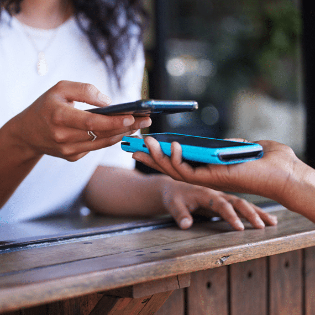 Two people exchange a digital payment by holding their smartphones close together over a wooden counter, highlighting the convenience of contactless transaction technology enabled by mobile banking.