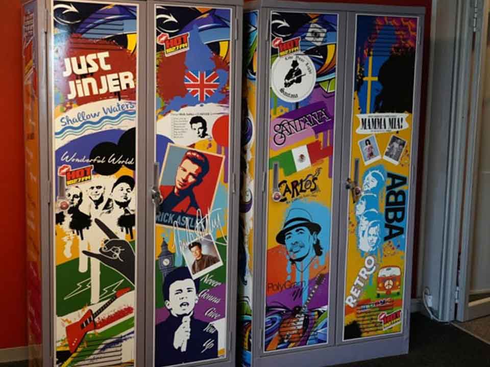 Two colorful lockers decorated with cutouts and images of music icons and bands, including ABBA, Carlos Santana, Ricky Martin, and themed graphics like flags, guitars, and the word RETRO in bold letters.