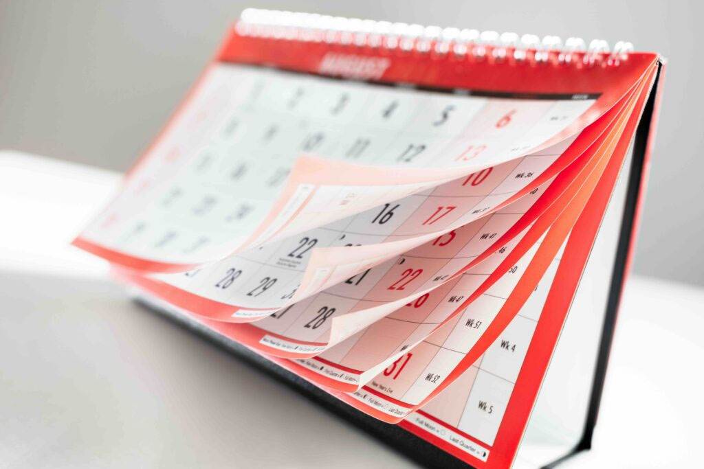 A close-up of a standing desk calendar with several pages fanned out, displaying dates and numbers in bold print, suggesting the passage of time or upcoming events.