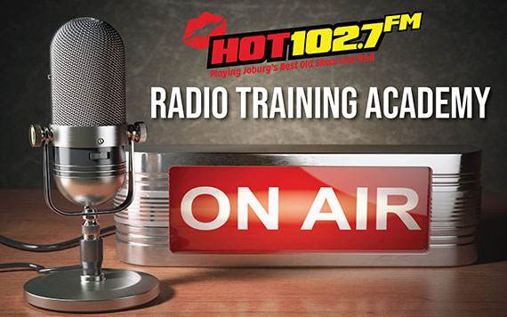 A vintage microphone sits next to an illuminated ON AIR sign. Above them is the logo for HOT 102.7 FM and the text RADIO TRAINING ACADEMY.