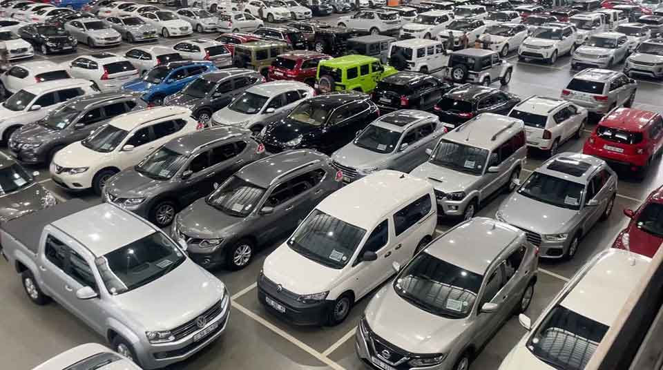 A crowded indoor car lot filled with rows of parked vehicles in various colors and models, including SUVs, trucks, and sedans, all neatly arranged side by side.