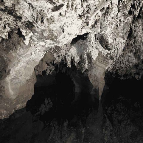 Rocky cave interior with jagged white and brown formations on the ceiling, reflected in a still pool of dark water below, evokes the mysterious and shadowy atmosphere of the famed Sterkfontein Caves.