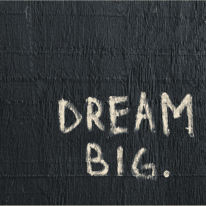 White painted text DREAM BIG. on a black textured wooden background.