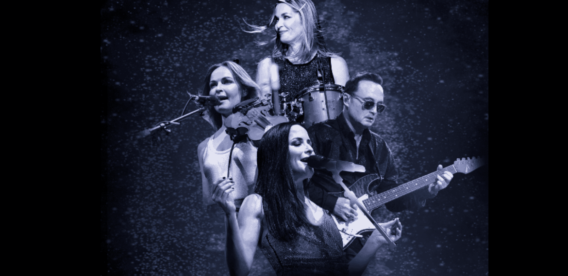 Four musicians perform on stage, reminiscent of The Corrs: three women singing while playing violin, drums, and guitar, with a man on electric guitar—all set against a starry, dark blue background.