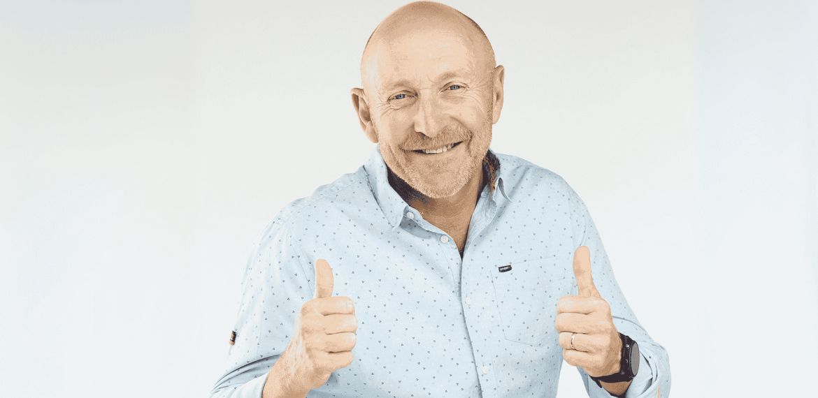 A smiling bald man wearing a light blue button-up shirt gives two thumbs up against a plain light background, showing he's clearly free from any brainrot.