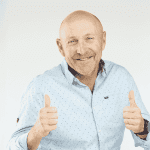 A smiling bald man wearing a light blue button-up shirt gives two thumbs up against a plain light background, showing he's clearly free from any brainrot.
