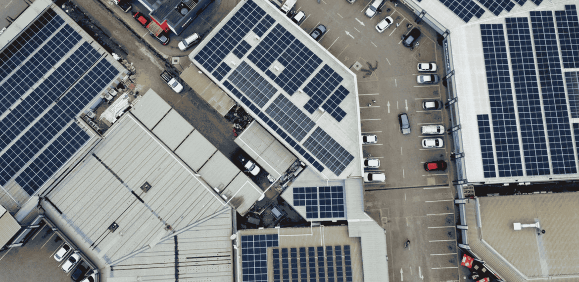 Aerial view of several large buildings with solar panels on their roofs and a parking lot filled with cars, highlighting new business opportunities in sustainable energy solutions.