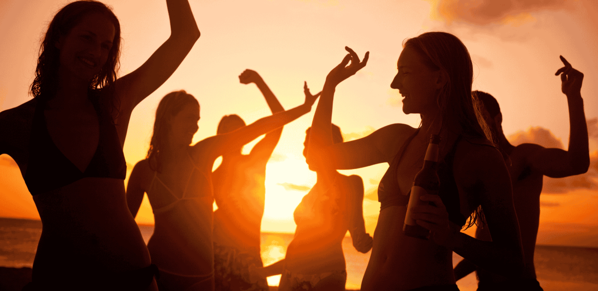 A group of people in swimwear dance and celebrate on the beach at sunset, one holding a bottle. The glowing orange sky creates vibrant silhouettes, reflecting new business opportunities in a lively coastal setting.