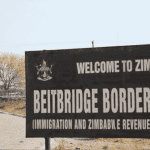 A large sign reads “Welcome to Zimbabwe. Beitbridge Border Post (Immigration and Zimbabwe Revenue Authority)” next to a paved road, with trees and dry grass in the background, highlighting potential business opportunities at this busy crossing.