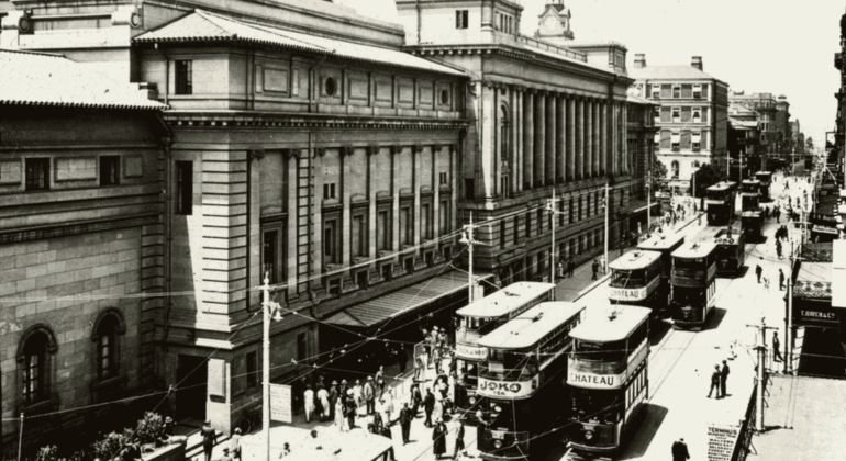 Historic black-and-white photo of a busy city street with several double-decker trams, people walking, and large classical buildings lining the road—like visual cover versions of vibrant urban life from another era.