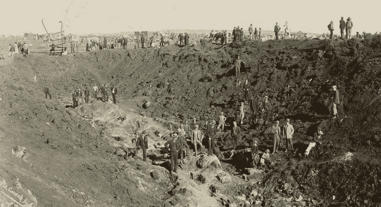 Historical photo of many people working in a large, deep excavation site—much like the vibrant eras Miriam Makeba witnessed—shows dirt mounds and workers scattered throughout the scene.