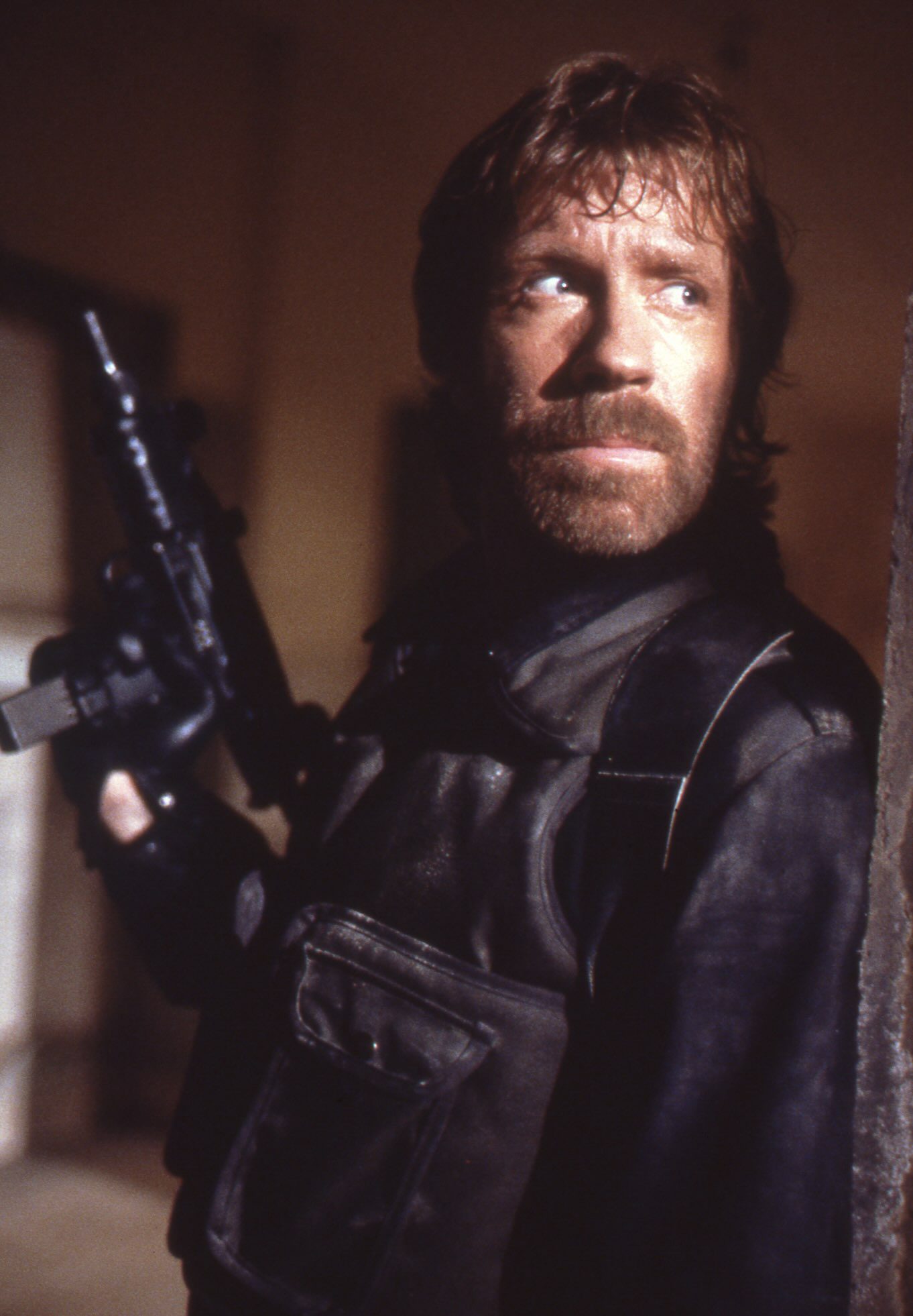 A bearded man in tactical gear holds a rifle and stands alert against a wall, scanning the dimly lit setting with intense focus—a true Matric operative on high alert.