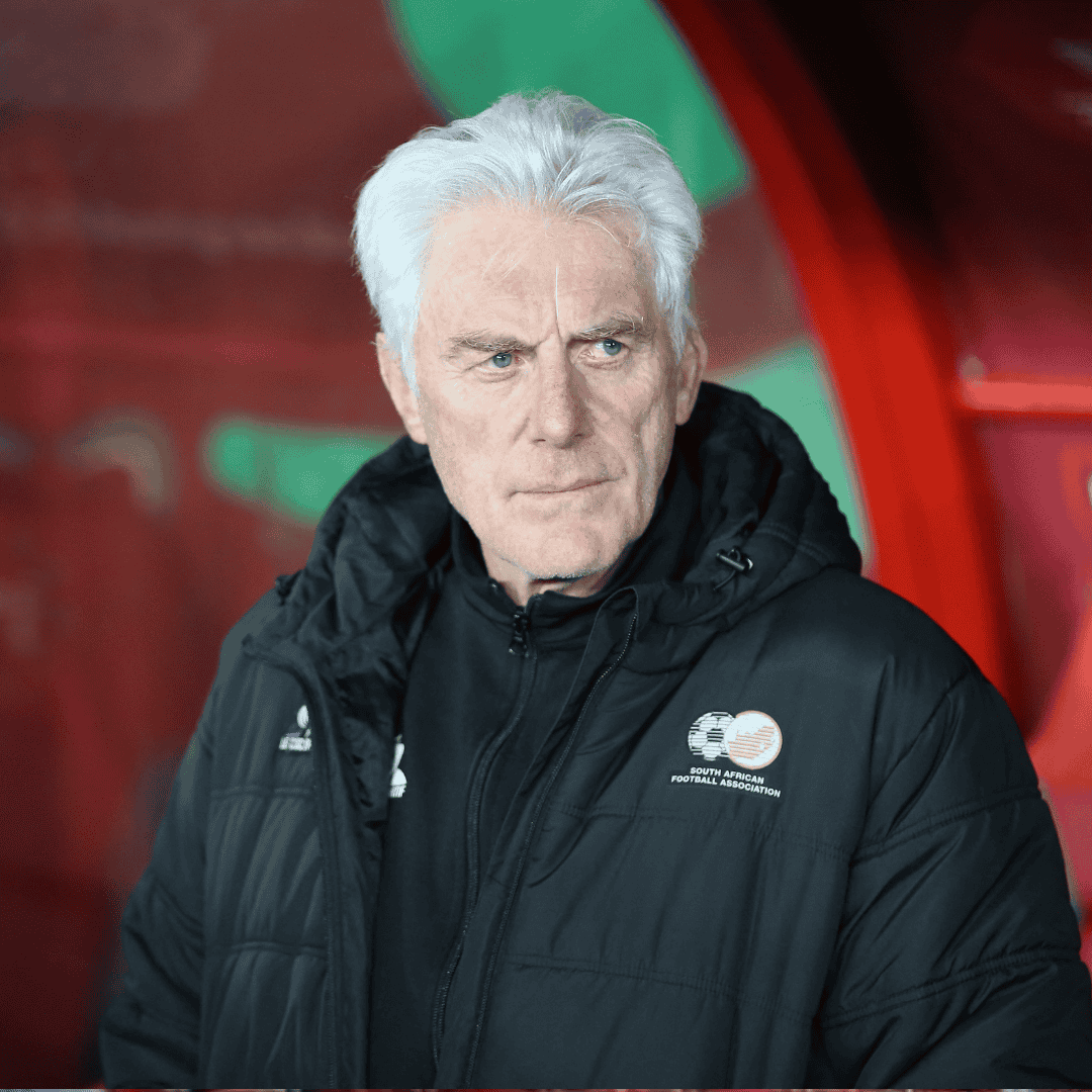An older man with white hair wearing a black jacket stands in front of a red background. The football-themed jacket hints at travel, and he looks to the side with a serious expression, as if planning his next getaway.