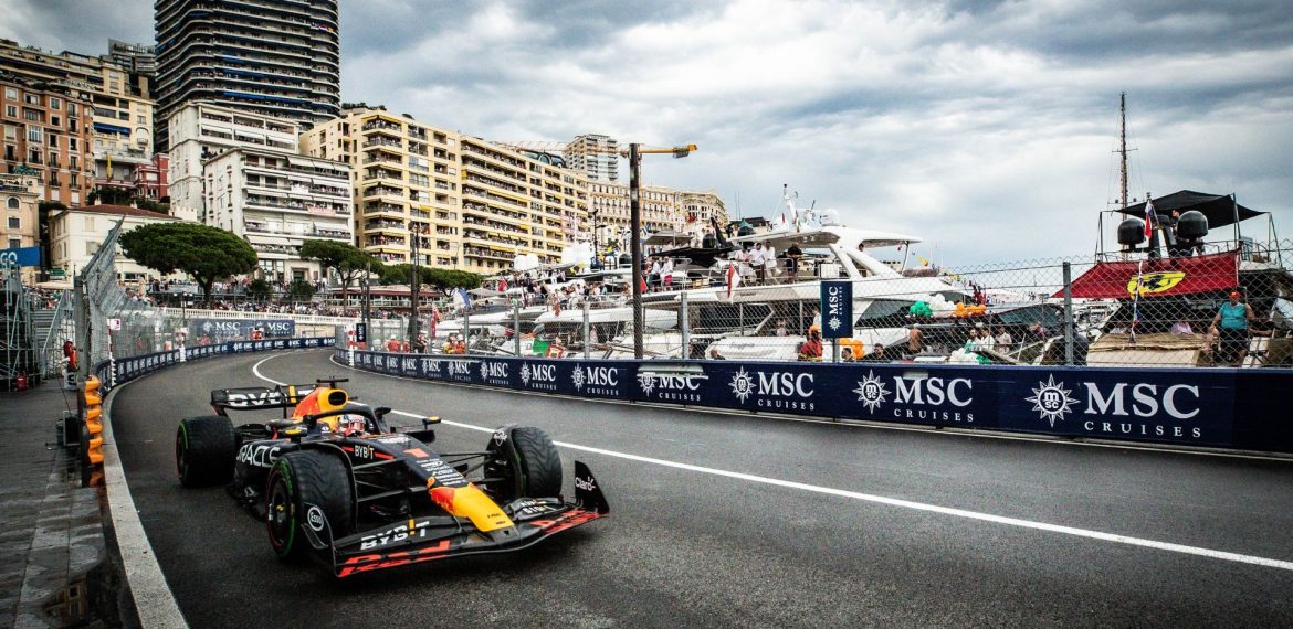 A Formula 1 car races along a street circuit by the waterfront, with tall buildings, yachts, and spectators in the background under a cloudy sky. MSC Cruises banners line the track, capturing the thrill of travel and a high-speed getaway.