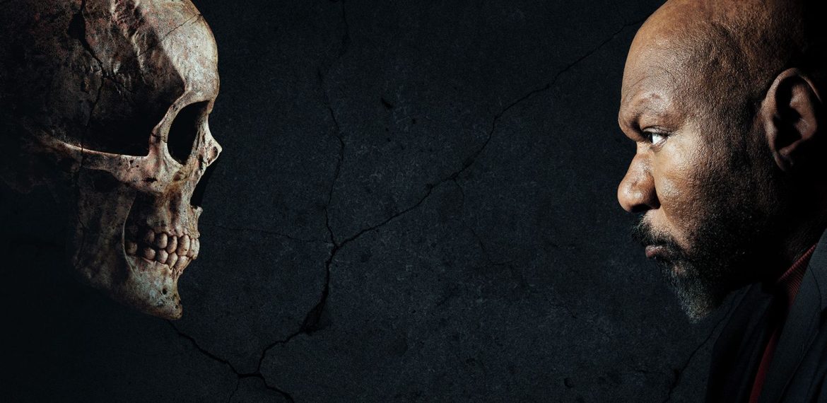 A man with a serious expression faces a human skull against a dark, cracked background, both in profile and staring intently at each other.